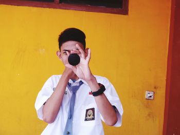 Portrait of young man photographing against yellow wall