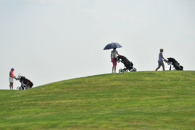 People riding bicycle on golf course against clear sky