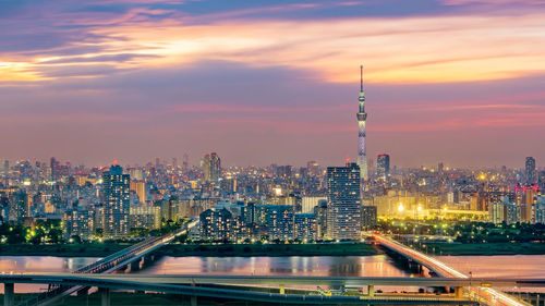 Illuminated buildings in city against sky during sunset