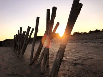 Wooden posts on beach against sky during sunset