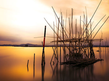 Silhouette of wooden posts in lake against sky during sunset