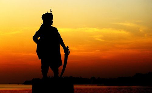 Silhouette of man statue against sea during sunset