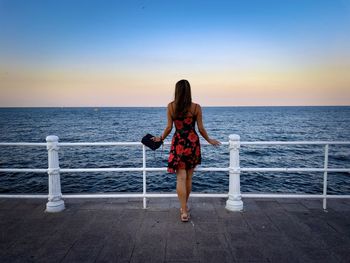 Rear view of woman wearing summer dress looking at the ocean at sunset