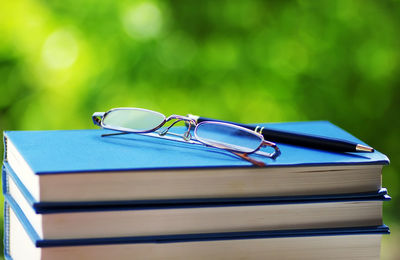 Close-up of eyeglasses and pen on books stack