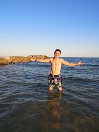 Portrait of shirtless man standing in sea against clear sky