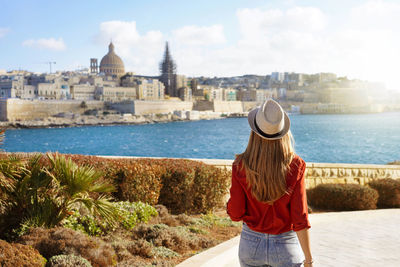 Woman with hat goes down along malta waterfront looking at beautiful cityscape of valletta, malta