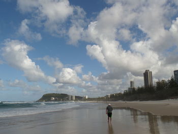 Man walking in sea against cloudy sky