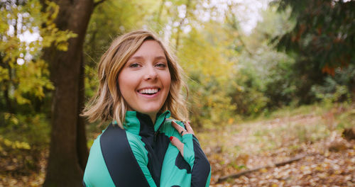 Portrait of smiling young woman standing in forest during autumn