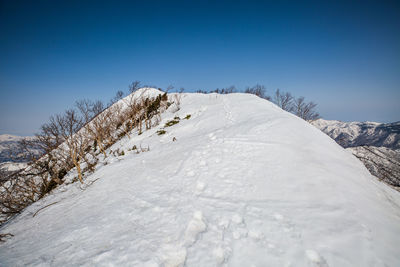 Snow covered landscape against clear blue sky