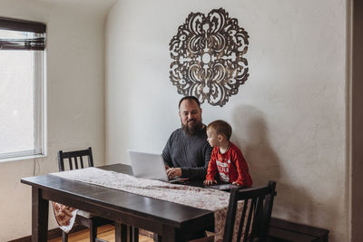 Wide view of father trying to work from home with toddler standing