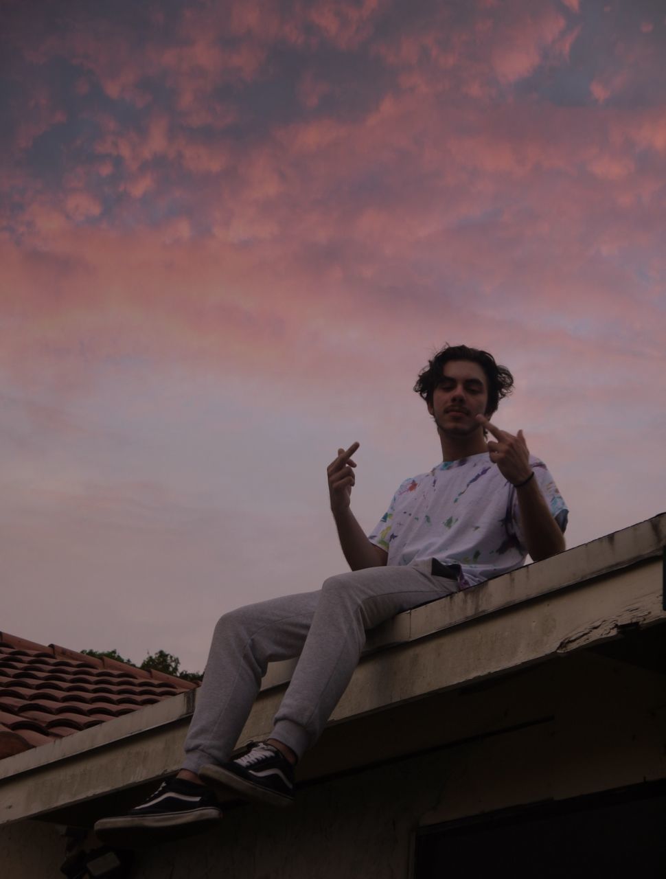 LOW ANGLE VIEW OF MAN SITTING ON ROOF AGAINST SKY