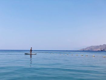 Man paddleboarding in sea against clear blue sky