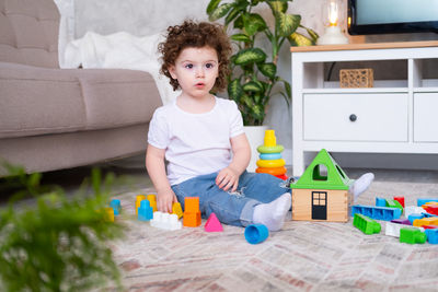 Cute girl playing with toys while sitting by sofa at home