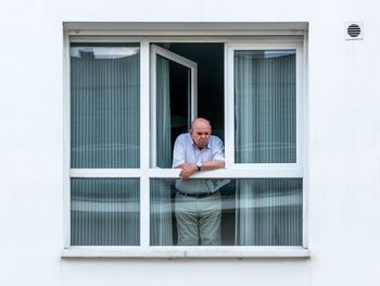 Portrait of man standing by window of building