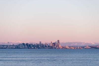 Sea by cityscape against clear sky during sunset