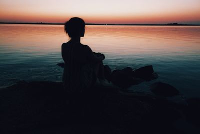 Rear view of silhouette woman sitting on rock at sunset