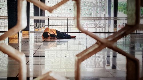 Man lying on tiled floor seen from metal grate