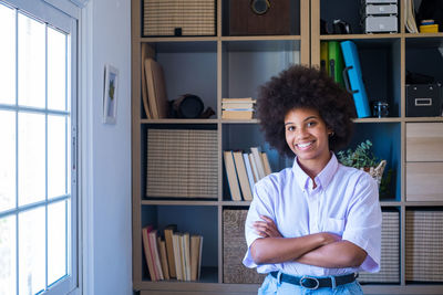 Portrait of smiling young woman standing against window