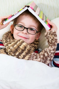 Portrait of boy holding book while lying down on bed at home