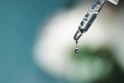 Pipette with serum, hyaluronic acid close up on blue background. drop falling from pipet. cosmetics