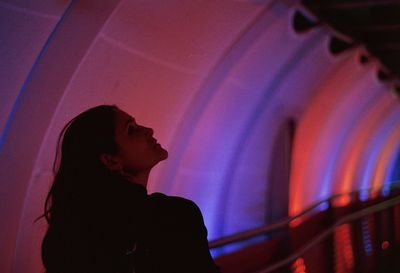 Woman looking away while standing in illuminated tunnel