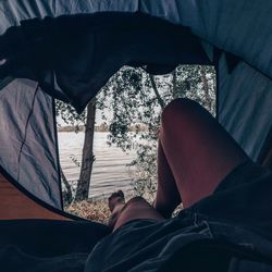 Low section of man relaxing by lake in tent