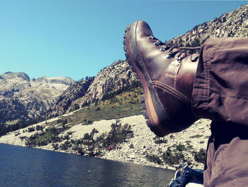 Low section of person by river against clear sky