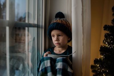 Young boy holding a cereal bowl looking out the window at christmas