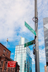 Low angle view of road sign and buildings against cloudy sky