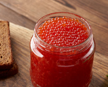 Full glass jar with red caviar on a brown wooden table, top view