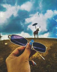 Midsection of person holding sunglasses against sky