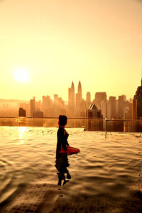 Woman standing in infinity pool against cityscape