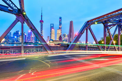 Light trails on bridge by buildings against sky in city