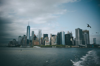 Sea and buildings in city against cloudy sky