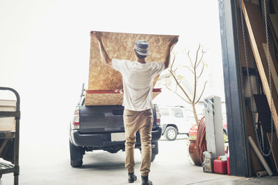 Rear view of man loading wooden planks in pick-up truck