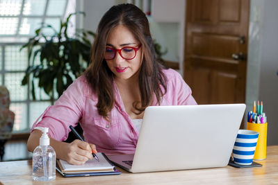 Young woman using phone while sitting on table