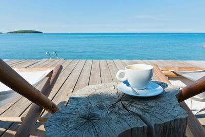 Close-up of coffee cup on table by sea against sky