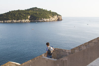 Rear view of man standing by sea against sky