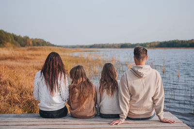 Rear view of people sitting on shore against sky