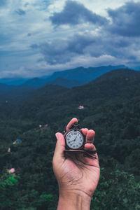 Cropped hand holding pocket watch against mountain