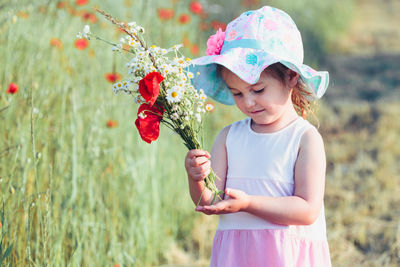 Full length of cute girl holding flower while standing on grass