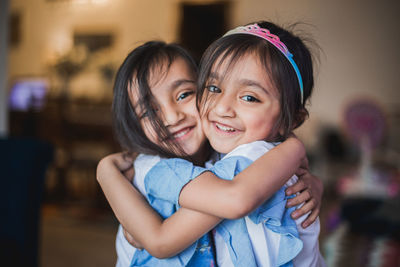 Portrait of smiling cute sisters embracing at home