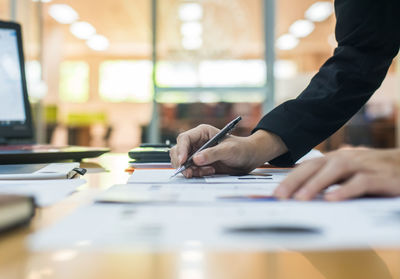 Cropped hands of businesswoman writing in paper at office