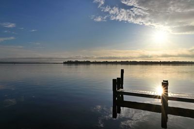 Wooden posts in lake against sky during sunset