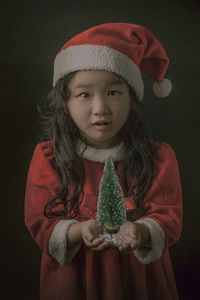 Close-up portrait of girl holding leaf against black background