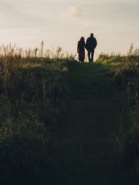 Rear view of couple holding hands while standing on field against sky