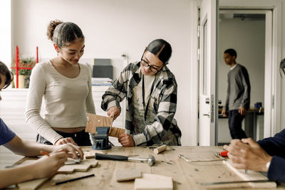 Teacher helping female teenage student while cutting wood during carpentry class