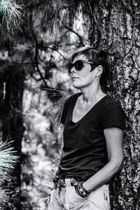 Portrait of beautiful young woman standing by tree trunk in forest