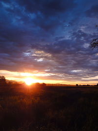 Scenic view of landscape against cloudy sky at sunset