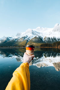 Midsection of person in lake against snowcapped mountains during winter
